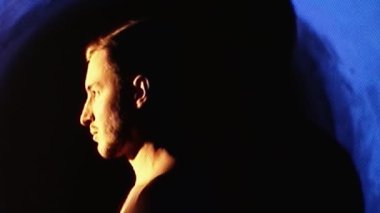 Glitched analog video. Nervous breakdown. Mood change. Silhouette of calm disturbed man suffering screaming clutching head in fire flame projector light with flicker noise.