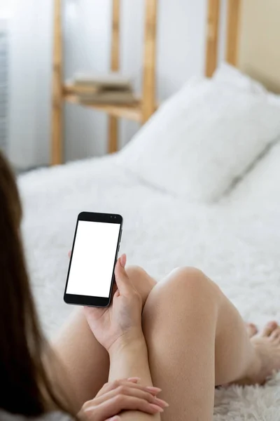 Mobile video. Online connection. Digital mockup. Unrecognizable relaxed woman looking smartphone with blank screen sitting bed in light room interior.