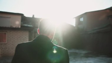 Man life. Future success. Leadership motivation. Back view of confident serious guy moving forward alone on cold urban street with brick houses on winter sunny day with lens flare.