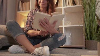 Enjoying reading. Inspired woman. Home leisure. Pretty smiling middle-aged lady sitting floor with interesting book in light room interior.