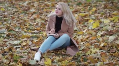 Romantic mood. Inspired woman. Diary moments. Pretty happy lady sitting on leaves ground making notes in notebook feeling joy slow motion.