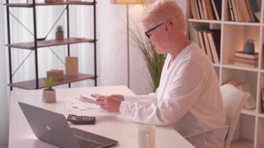 Investment income. Retirement business. Money management. Happy mature woman counting pension fund savings on calculator at home desk.