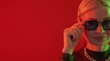 Sunglasses fashion. Stylish elderly. Neon light advertisement. Trendy happy mature woman winking eye in fluorescent glow red copy space.