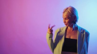 Advertising woman. Product promotion. Best offer. Happy stylish senior lady pointing aside on bright neon light gradient empty space.