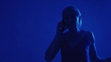 Emergency call. 911 help. Danger assistance. Scared worried senior woman contacting rescue center service on phone in flashing alarm light at night copy space.