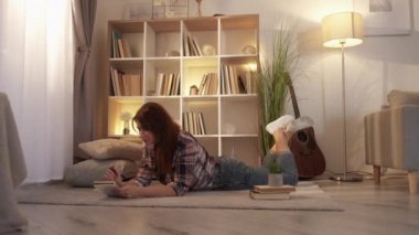 Female diary. Romantic mood. Home leisure. Pretty middle-aged casual woman laying floor making notes in cozy atmosphere in light room interior.