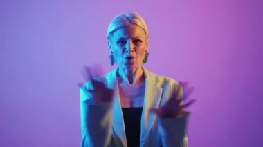 No way. Refusing woman. Stop gesture. Serious confident senior female showing hands rejection expression in purple bright neon light.