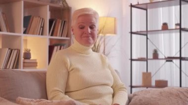Senior loneliness. Sad retirement. Elderly depression. Dreamy mature woman hugging pillow missing family on couch at home living room.