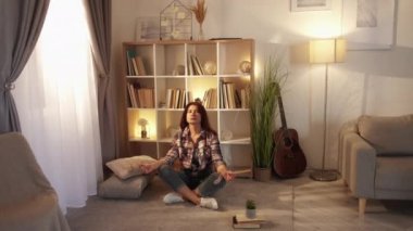 Inspired meditation. Tranquil woman. Home relax. Calm peaceful middle-aged lady sitting floor lotus pose in light room interior.