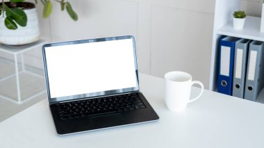 Computer mockup. Online technology. Digital life. Opened laptop with blank screen staying on work desk with cup of coffee in light room interior.