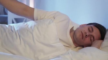 Restless sleep. Bad dream. Bedtime anxiety. Disturbed tired exhausted guy with closed eyes tossing and turning lying in uncomfortable bed at night.