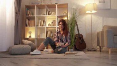Romantic mood. Dreamful woman. Home leisure. Beautiful middle-aged casual lady sitting floor making notes in cozy atmosphere in light room interior.