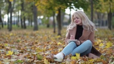 Muse inspiration. Romantic woman. Diary moments. Pretty smiling lady sitting on leaves ground making notes in notebook feeling joy.