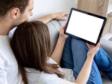 Mobile mockup. Beloved couple. Home movie. Relaxed unrecognizable man and woman watching tablet computer with blank screen in light room interior.
