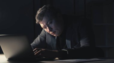 Vertical video. Late work. Inefficient man. Project deadline. Exhausted male employee working laptop in dark home office interior.