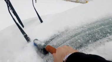 Winter snow season. Car owner cleaning his auto windshield in the morning using brush
