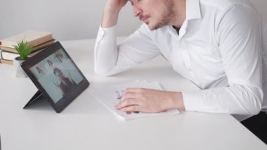 Sıkıcı bir ders. Yorgun adam. İnternetteki konferans. Zarif erkek, aydınlatma odasının iç tarafındaki tablet bilgisayarda sanal görüşme yapmaktan yorgun düşüyor..