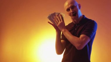 Büyük para. Neşeli adam. Zengin heyecanı. Mutlu komplocu etkileyici adam sarı turuncu ışıklı arka planda nakit para gösteriyor..