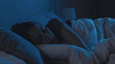 Dikey video. Gece uykusu. Rahat kadın. Uyku vakti. Yorgun ve gözleri kapalı bir kadın, karanlık bir evde yatakta yatıyor..