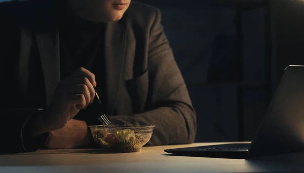 Vertical video. Night dinner. Busy man. Business project. Hungry business guy eating vegetable salad looking laptop sitting work desk in dark room interior.