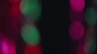 Bulanık neon halkalar. Bokeh ışığı üstüste biniyor. Gece partisi ışıltısı. Odaklanmamış pembe yeşil yuvarlak lekeler koyu siyah soyut arka planda parlıyor.