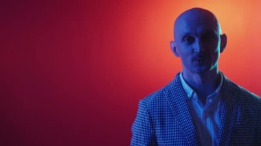 Aktör monoloğu. Pozitif adam. Neon ışıklı portre. Gülümseyen adam, sıradan bir görünüm takınıp kırmızı arka planda kameraya konuşuyor..