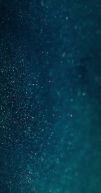 Bulanık parlayan su. Parçacık arkaplanı. Bokeh ışık daireleri. Odaklanamayan mavi turuncu renkli baloncuklar soyut koyu bir örtüde yüzüyor. Dikey video. RED Sinema Kamerasında Çekim.