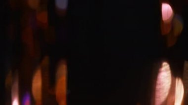 Bokeh ışığı üstüste biniyor. Bulanık parıltılar. Gece aydınlatması. Odaklanmamış turuncu mavi yuvarlak payetli parıltı koyu siyah soyut arkaplanda parlıyor.