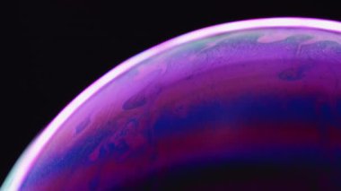 Gökkuşağı kabarcığı. Makro küre. Akışkan sanat. İçinde mavi mor boya bulunan renkli sabun ampulü siyah arkaplanda beyaz bir çizgi çiziyor..