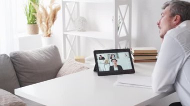 Sıkıcı eğitim. Hayalperest adam. Online konferans. Düşünceli, yorgun erkek penceresi aydınlatma odasının iç tarafındaki tablet bilgisayarda sanal bir toplantı yapıyor..