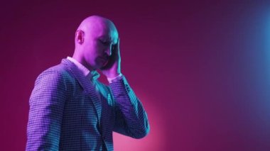 Baş ağrısı çekiyor. Bitkin bir adam. Neon ışıklı portre. Zarif adam elini pembe arka plan fotokopi alanının üzerinde tutarken kötü hissediyor..