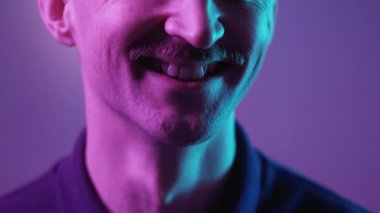Mutlu bir hayat. Neşeli adam. Neon ışıklı portre. Tanımlanamayan, içten gülümseyen, başını eğip menekşe mavisi arka planda poz veren adam..