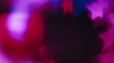 Renkli bokeh parıltısı. Işık parlaması üstüste biniyor. Yıldız deseni parlaklığı. Koyu siyah soyut arkaplan üzerinde odaklanmış neon mavisi kırmızı parıltı hareketi.