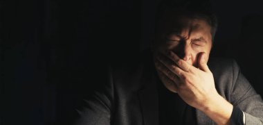 Dikey video. Gece uykusuzluğu. Yorgun adam. Fazla mesai. Yorgun, uykulu iş adamı esniyor. Koyu lamba odasının iç tarafında oturuyor..