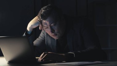 Dikey video. İşkolik yaşam tarzı. Yorgun adam. Projenin son teslim tarihi. Uykulu erkek çalışan, karanlık ofis içinde dizüstü bilgisayarda çalışıyor..