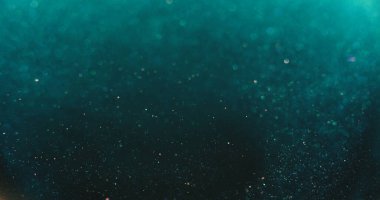 Bokeh ışığı üstüste biniyor. Bulanık parıltı dokusu. Işıldayan su kabarcıkları. Odaklanmamış verdigris yeşil mavi turuncu renk parçacıkları koyu soyut arkaplanda.