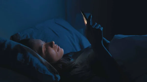 垂直ビデオ デジタル中毒だ 疲れた女 オンライン生活 薄暗い影の部屋のインテリアにスクロールベッドスクロールスマートフォンを敷設眠れない女性 — ストック写真