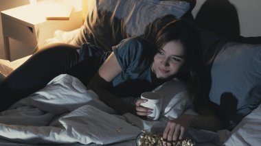 Komedi şovu. Uykusuzluk gecesi. Ev tatili. Mutlu kadın komik film seyrediyor patlamış mısır yiyor çay içiyor, yatak odasının içini karartıyor..