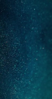 Bulanık parlayan su. Parçacık arkaplanı. Bokeh ışık daireleri. Odaklanamayan mavi turuncu renkli baloncuklar soyut koyu bir örtüde yüzüyor. Dikey video. RED Sinema Kamerasında Çekim.