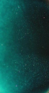 Bokeh ışık arkaplanı. Bulanık parıltı. Suda yüzen kabarcıklar. Odaklanmamış verdigris yeşil turuncu renkli parçacıklar koyu soyut doku. Dikey video. RED Sinema Kamerasında Çekim.