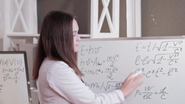 Video dersi. İnternet öğretmenliği. Uzaktan bilimsel araştırma. Sanal sınıfta beyaz tahtada denklem çözen zeki öğretmen kadın..