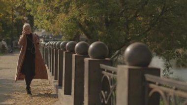 Romantik sonbahar. Mutlu kadın. Mobil müzik. Güzel gülümseyen orta yaşlı bir bayan park yolunda yürüyor ve dans ediyor. Akıllı telefon ve telli başlık ile neşe içinde..