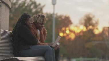 Çevrimiçi iletişim. Pozitif çift. Görüntülü arama. Mutlu siyah kadın ve erkek bir arada oturmuş gün batımında dizüstü bilgisayarla konuşuyorlar..