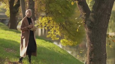 Sonbahar sezonu. Romantik kadın. Gündüz tatili. Oldukça mutlu orta yaşlı bir kadın Park Gölü 'nde kalıyor. Bir fincan kahve ve kitapla doğanın tadını çıkarıyor..