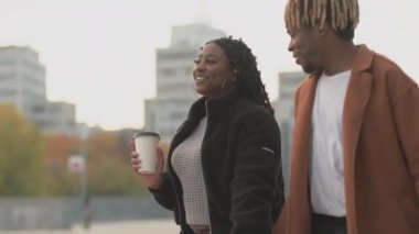Güzel bir hafta sonu. Sevgili çift. Alışveriş zamanı. Gülümseyen siyah kadın ve erkek bir fincan kahve ve alışveriş çantasıyla birlikte sokakta yürüyorlar..