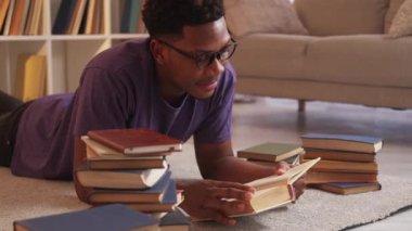 Boş vakitleri değerlendiriyorum. Hafta sonu çalışması. Zekice bir hobi. Rahat akıllı erkek öğrenci, oturma odasının iç kısmında açık bir kitapla yerde yatıyor..