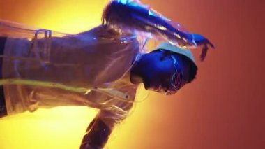 Dikey video. Siber punk partisi. Disko neşesi. Neon ışığı, LED gözlükle turuncu renk gradyan arka planda dans eden adamı eğlendiriyordu..