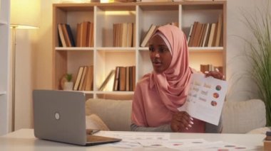 Proje sunumu. İlham verici bir kadın. Çevrimiçi toplantı. Doğulu kadın tesettürlü. Laptop 'a rapor veriyor. Işık odası iç tarafında oturuyor..