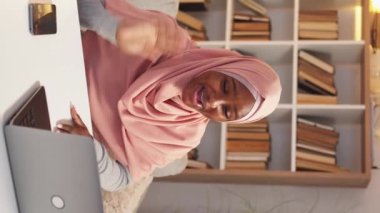 Dikey video. Çevrimiçi toplantı. İlham verici bir kadın. Sanal bağlantı. tesettürlü gülümseyen bayan dizüstü bilgisayardaki arkadaşlarını selamlıyor..