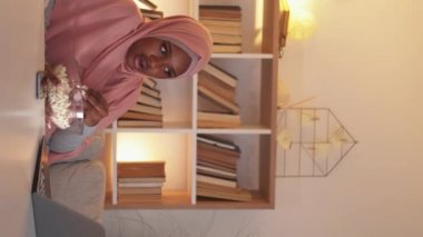 Dikey video. Çevrimiçi film. Şok olmuş kadın. Ev tatili. Şaşırmış, tesettürlü kadın dizüstü bilgisayarda beklenmedik bir durumla karşılaştı ve iç mekanda patlamış mısır yedi..